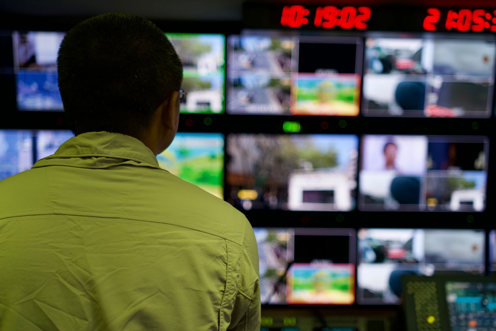 Uma pessoa em uma sala de monitoramento, telas com dados de rede — vigilância silenciosa enquanto a cidade dorme.